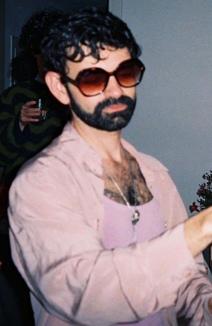 thiago at a party in big tinted sunglasses and an open pink shirt, a friend with a drink behind him